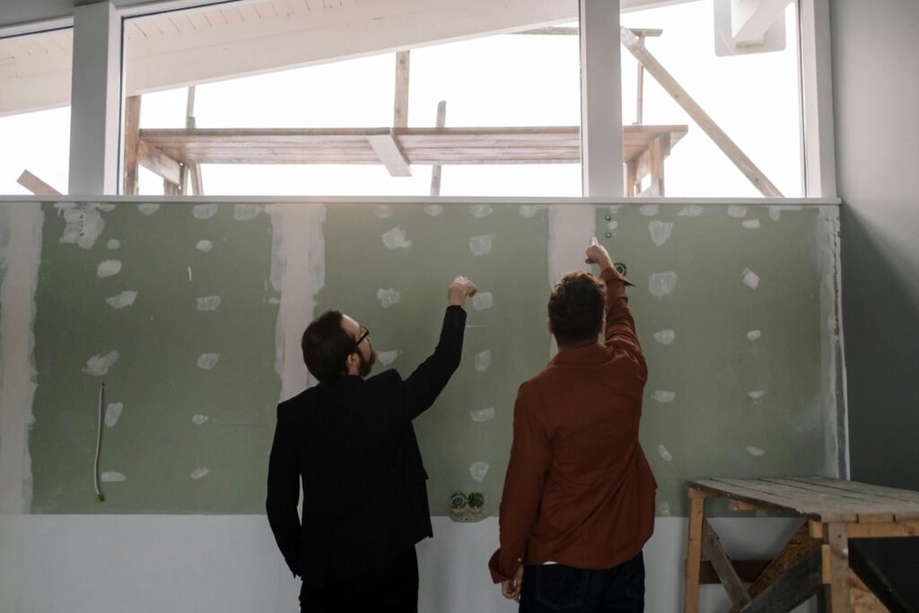 Two men discussing and pointing at an interior wall during a renovation project.